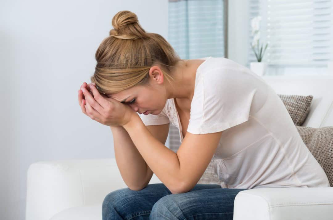 A woman sat down with her head in her hands, with a look of stress and worry on her face.